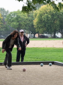 Patron throws bocce ball on court, others watch.